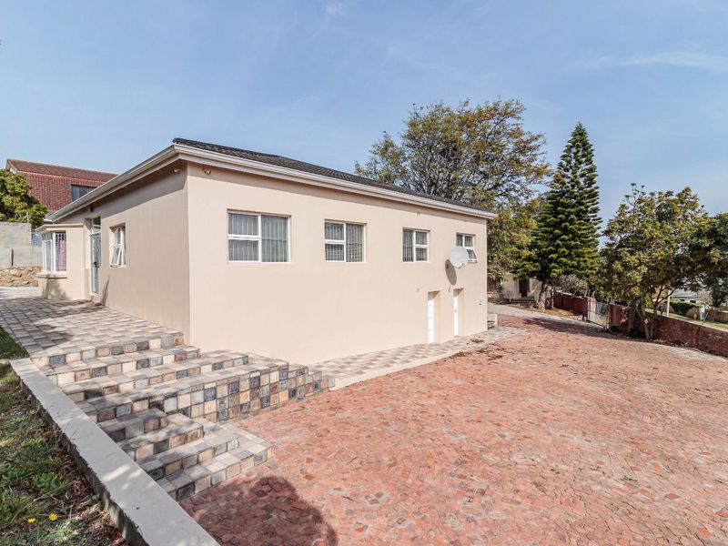 Rear view of the property featuring a paved driveway, tiled exterior staircase, and well-maintained exterior walls with sliding windows.