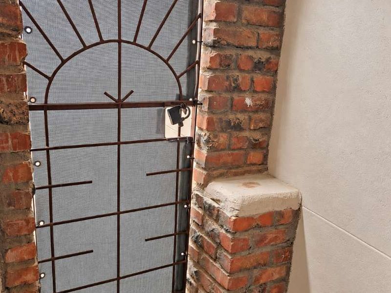 A secure arched entryway featuring exposed brickwork, a decorative metal security gate, and tiled flooring.