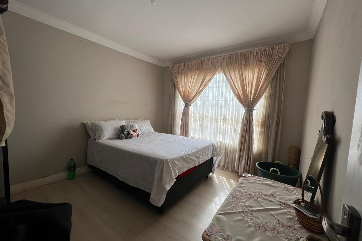 A bedroom featuring light-toned laminate flooring, neutral wall paint, and floor-to-ceiling curtains covering the window.