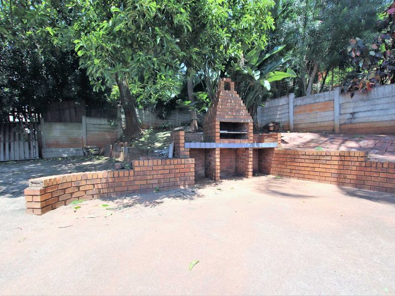 Outdoor patio area featuring a built-in brick braai, concrete flooring, and a surrounding brick retaining wall, set within a garden space.