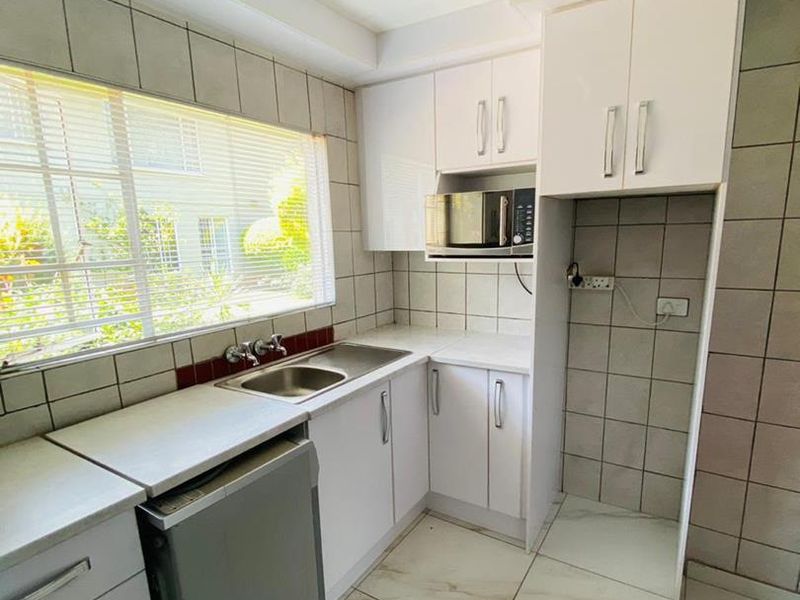 A clean, functional kitchen featuring white built-in cabinetry, tiled splashbacks, double bowl sink, and dedicated appliance space with tiled flooring throughout.