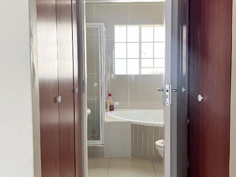 A view through a hallway with built-in cupboards into a bathroom featuring a corner bathtub, shower enclosure, and tiled finishes.