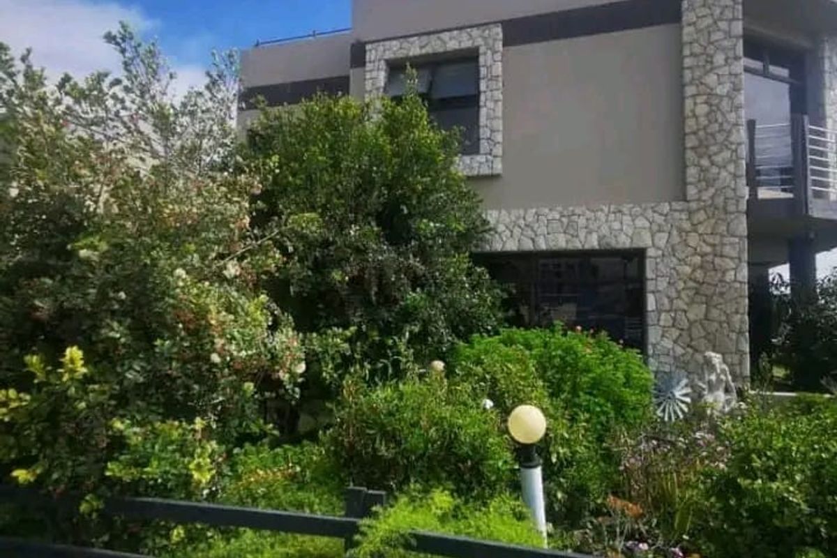 A modern two-story residential property featuring stone cladding accents, large windows, and a well-established garden with a perimeter fence.