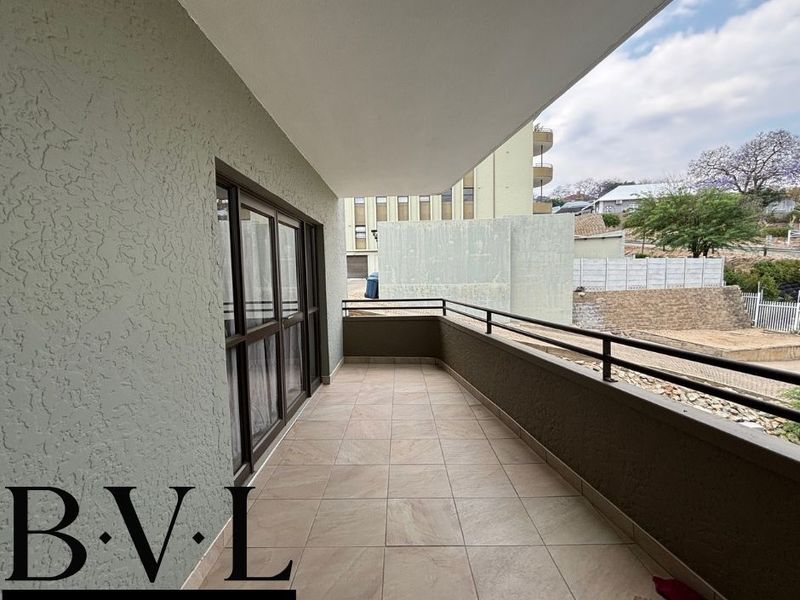 A spacious covered balcony featuring tiled flooring, a metal safety balustrade, and sliding glass door access to the apartment interior.