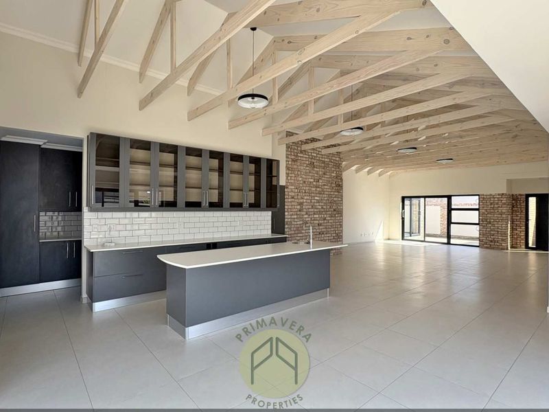 Spacious open-plan living area featuring exposed timber trusses, brick feature walls, and a modern kitchen with a central island and sleek cabinetry.