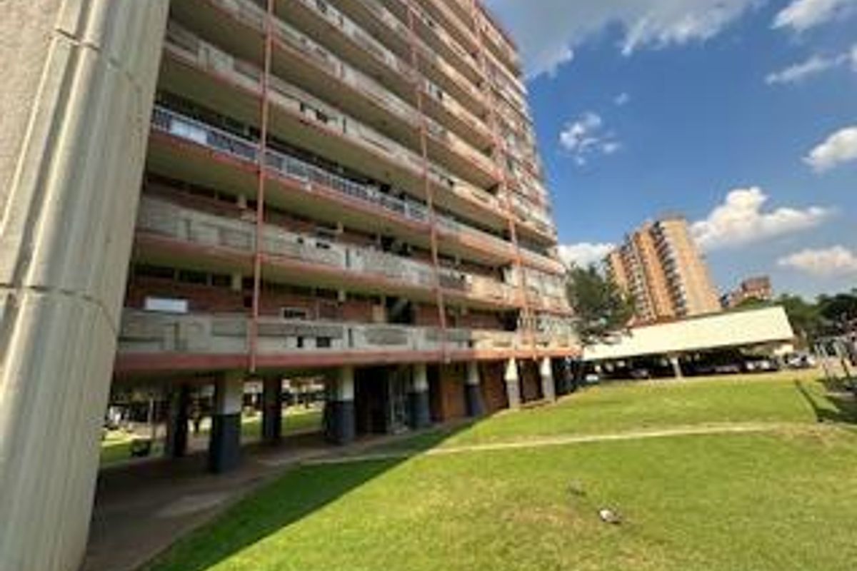 Exterior view of a multi-story apartment building featuring open-air balconies and a surrounding lawn area.