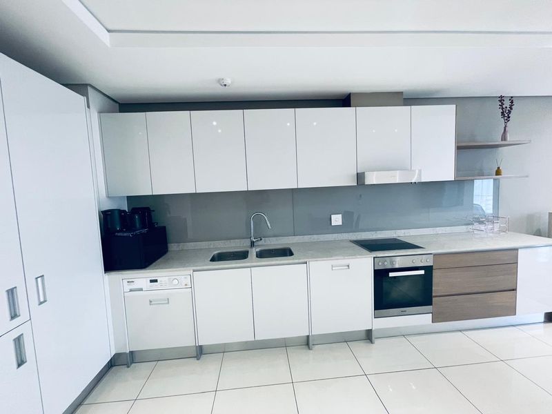 Modern kitchen featuring glossy white cabinetry, integrated appliances, stone countertops, glass splashback, and sleek tiled flooring in a clean, contemporary design.