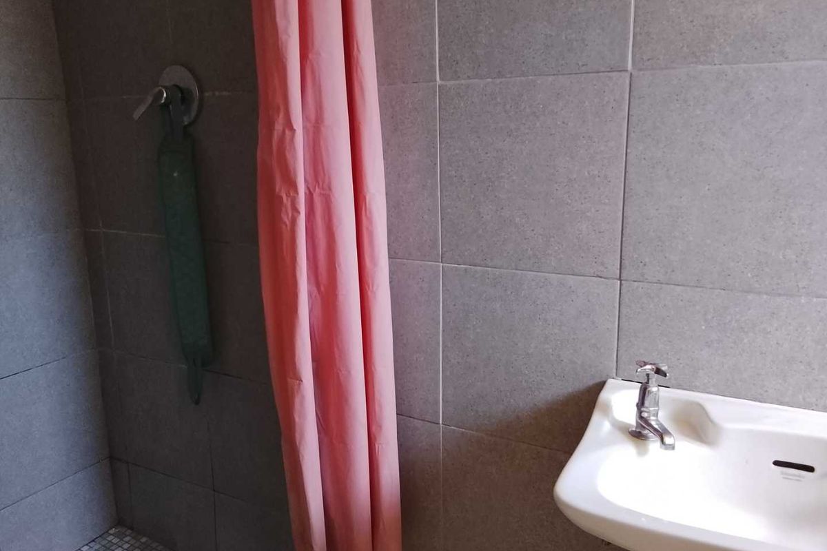 A functional bathroom featuring grey wall tiling, a wall-mounted basin, and a shower area with a curtain.