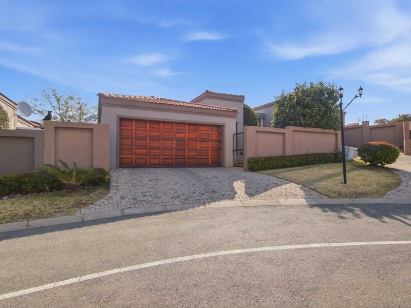 Front exterior view of the property featuring a wooden garage door, paved driveway, and secure perimeter walling.