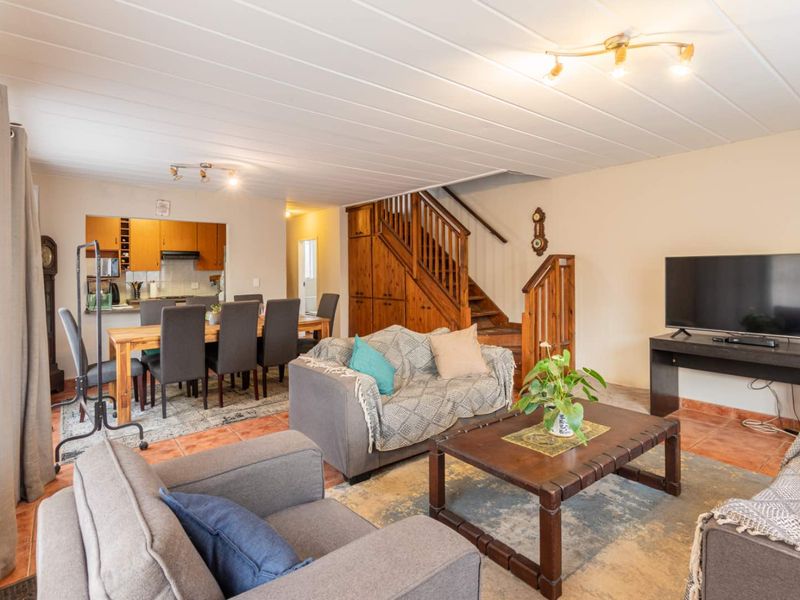 Open-plan living and dining area featuring tiled floors, a wooden staircase, and an integrated kitchen space with built-in cabinetry.