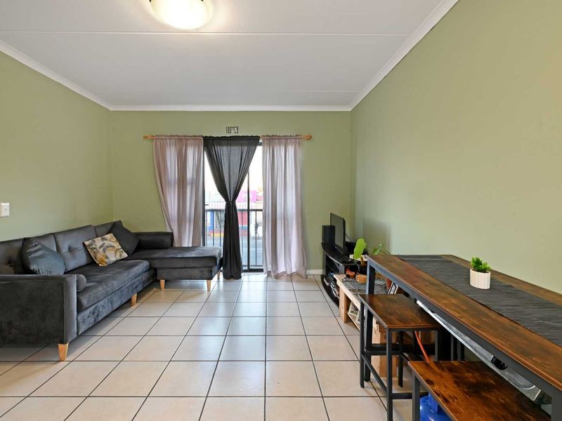 A living room featuring tiled flooring, neutral green walls, and a sliding glass door providing access to a balcony.