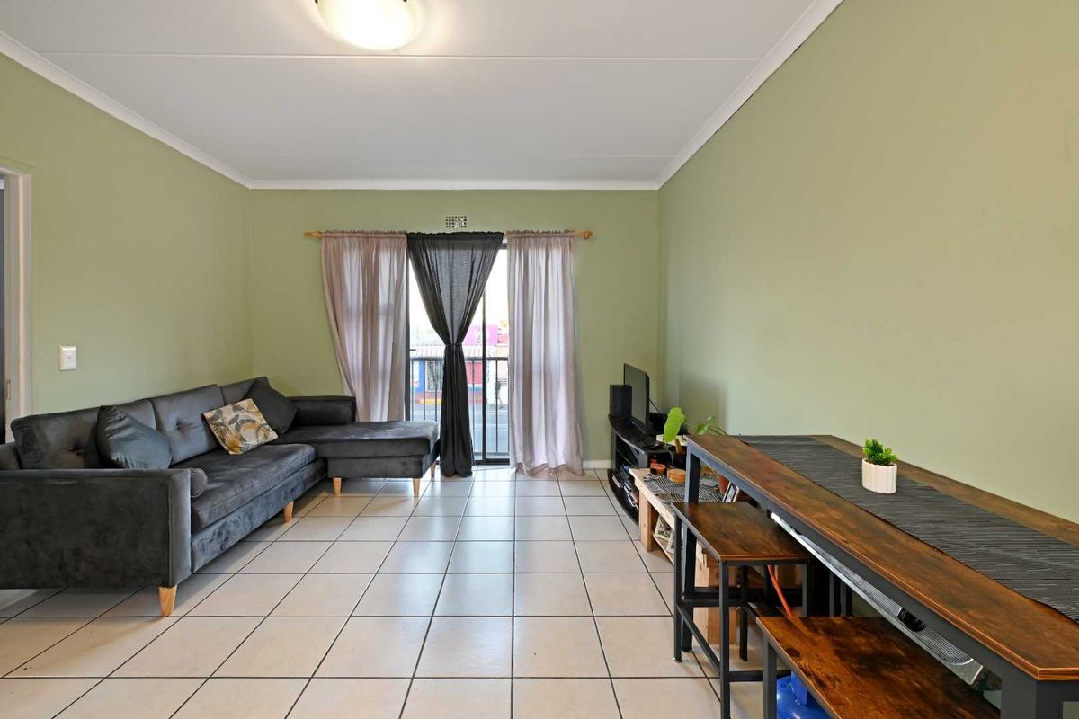 A living room featuring tiled flooring, neutral green walls, and a sliding glass door providing access to a balcony.