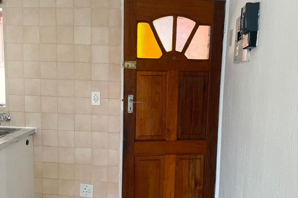 A functional kitchen area featuring tiled splashbacks, a sink, and a traditional timber door with decorative stained glass inserts.