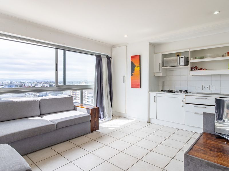 Open-plan living area featuring a compact kitchen with built-in cabinetry, gas hob, and large windows offering expansive city views.