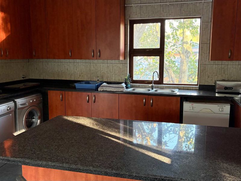 A functional kitchen featuring dark granite countertops, warm-toned wooden cabinetry, a central island, and a double basin sink with natural light.