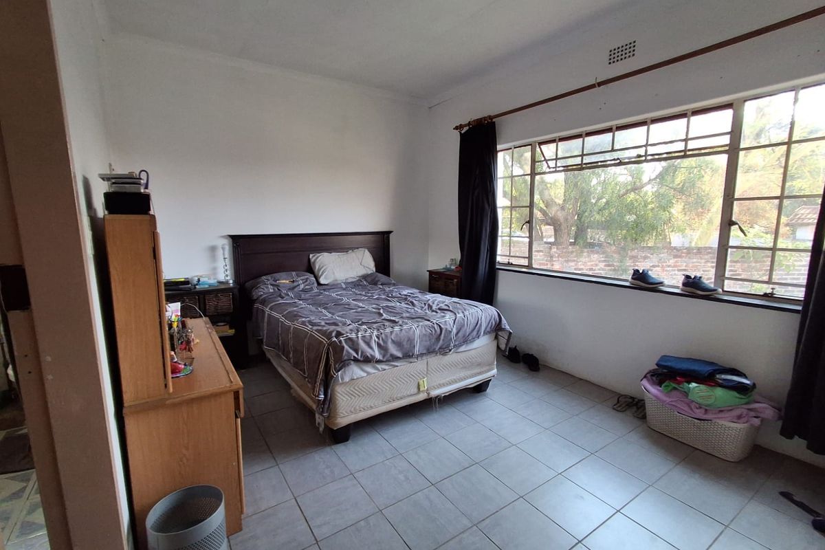 A bedroom featuring tiled flooring and a large window that provides natural light. The space is functional but would benefit from cosmetic updates.
