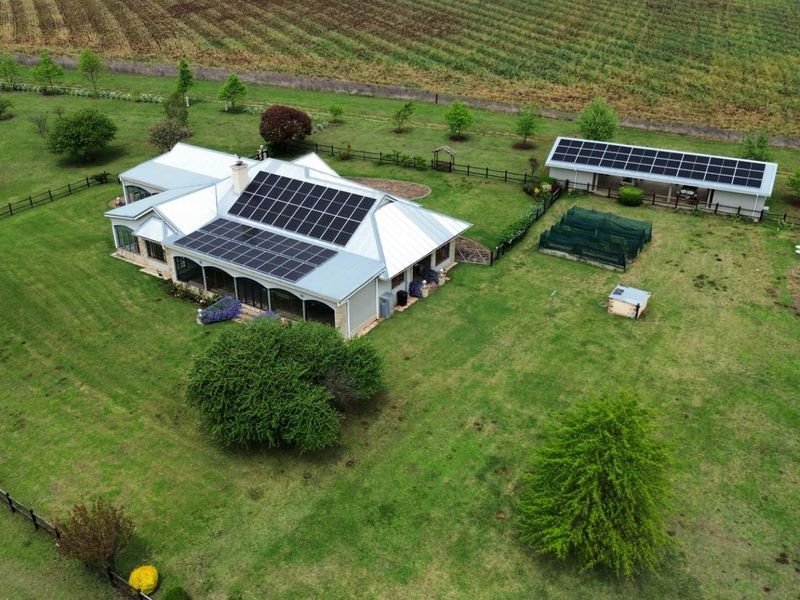 Aerial view of a farm property featuring a main residence with solar panels, a covered patio, and a separate outbuilding set within expansive grounds.