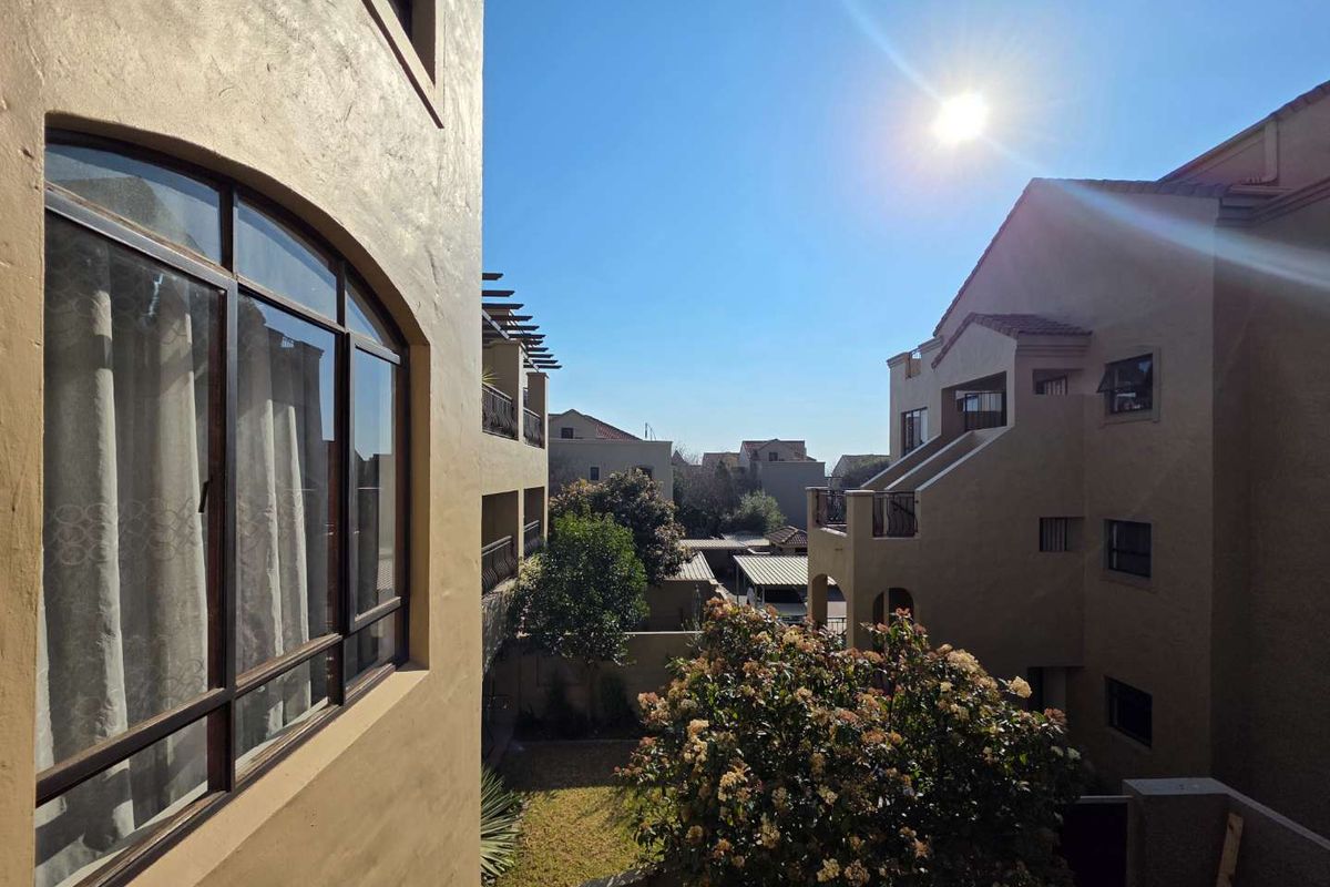 View of the apartment complex exterior showing the rear facade, balconies, and landscaped courtyard area under a clear sky.