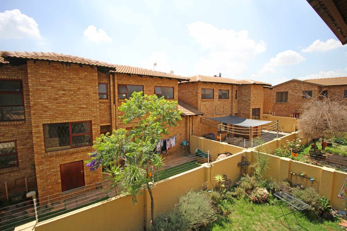 An elevated view of the rear exterior of a townhouse complex, featuring face-brick facades, private garden spaces, and boundary walls with security fencing.