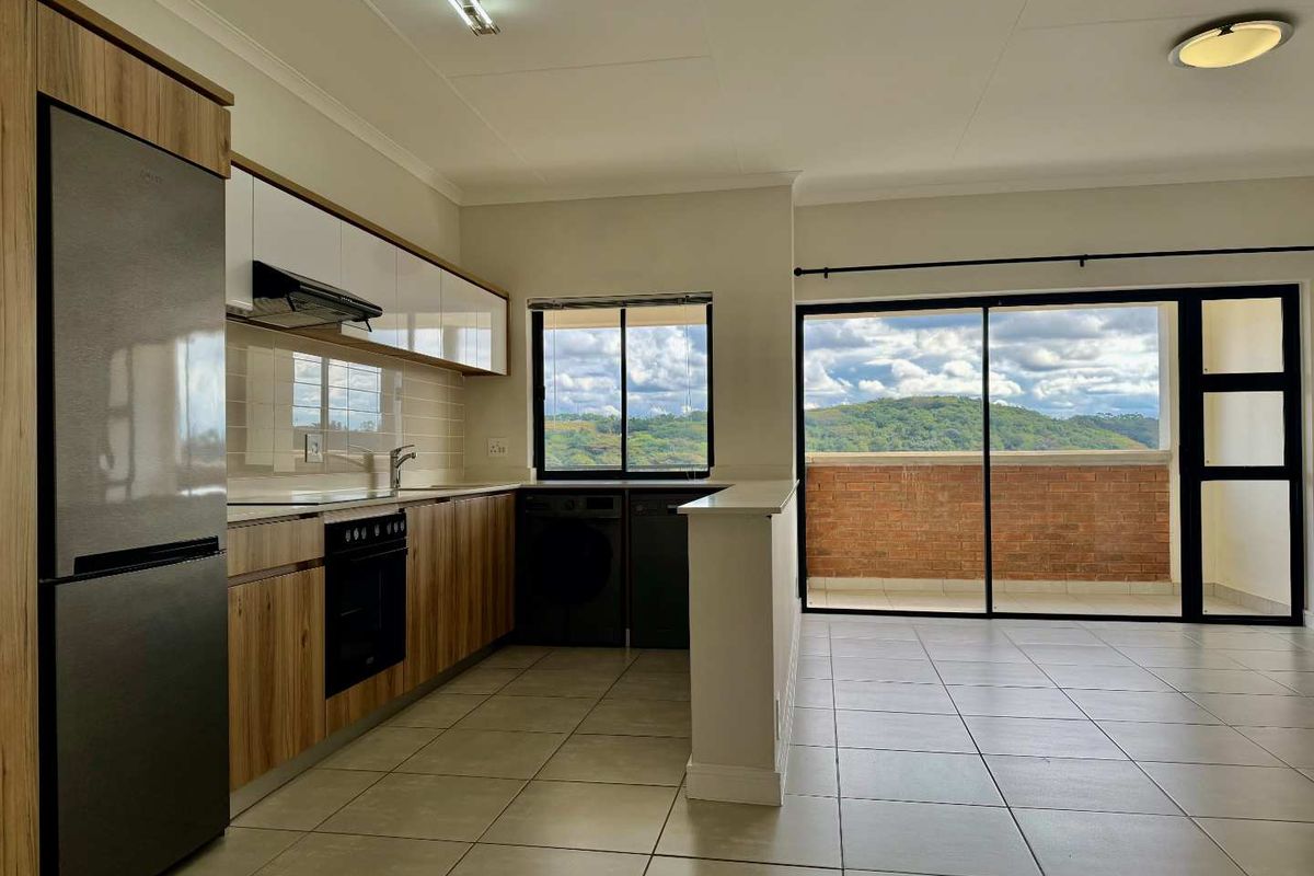 Modern open-plan kitchen and living area featuring sleek cabinetry, tiled floors, and large sliding doors opening to a balcony with scenic views.