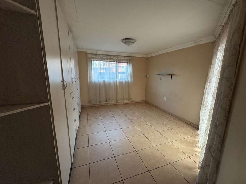 A vacant bedroom featuring tiled flooring, built-in cupboards, and a window with security bars, offering a neutral canvas for potential updates.