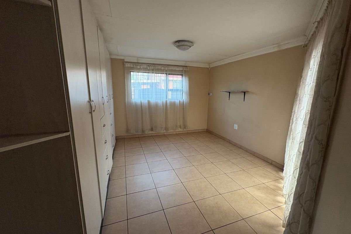 A vacant bedroom featuring tiled flooring, built-in cupboards, and a window with security bars, offering a neutral canvas for potential updates.