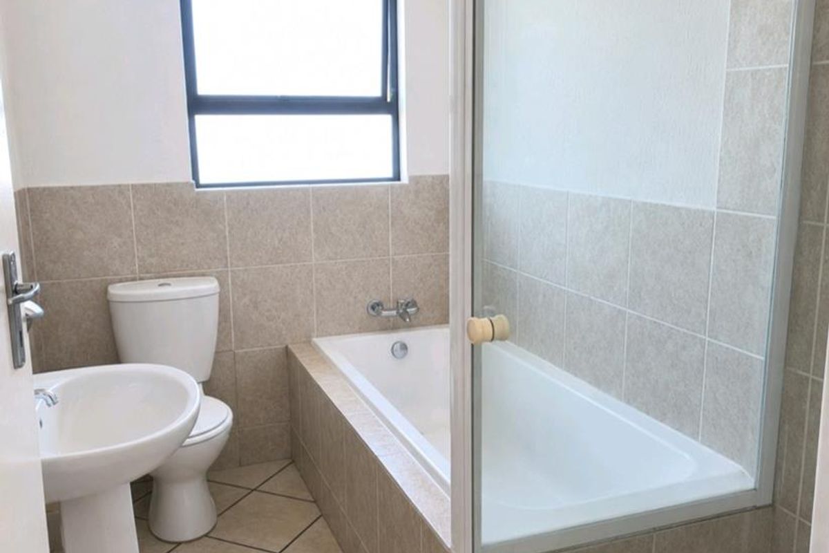 A clean, functional bathroom featuring a pedestal basin, toilet, and a combined bathtub with a glass-enclosed shower area.