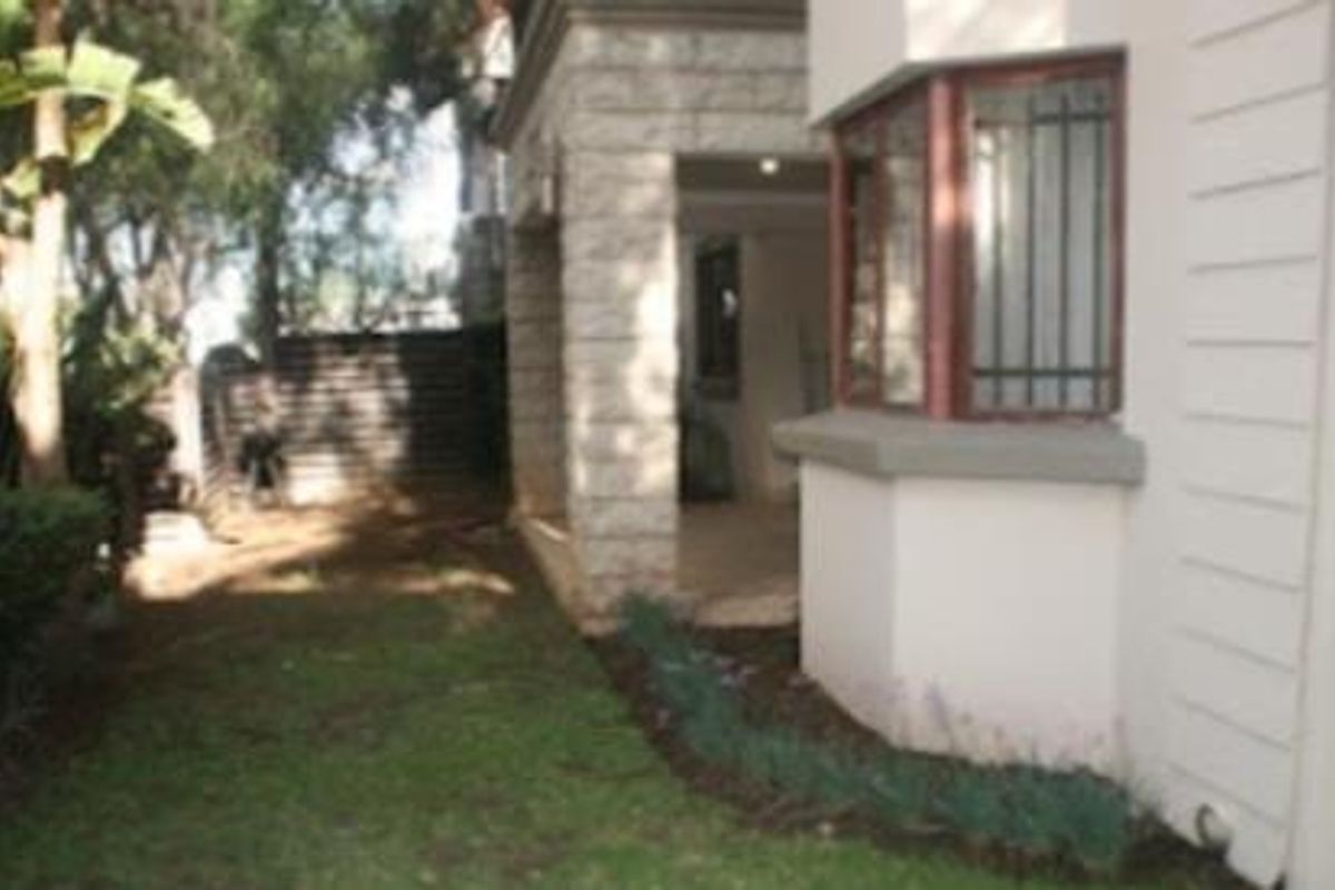 A view of the rear exterior of the apartment, featuring a small garden area, a covered patio, and a bay window with security bars.