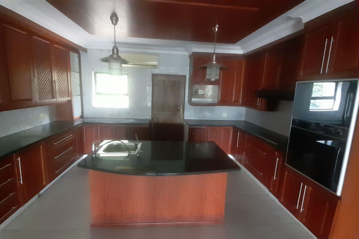 Spacious kitchen featuring dark wood cabinetry, a central island with a sink, granite countertops, and built-in oven.