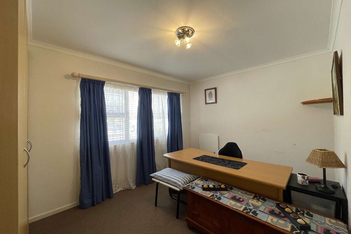 A functional bedroom or home office space featuring neutral walls, carpeted flooring, and a window with fitted curtain rod.