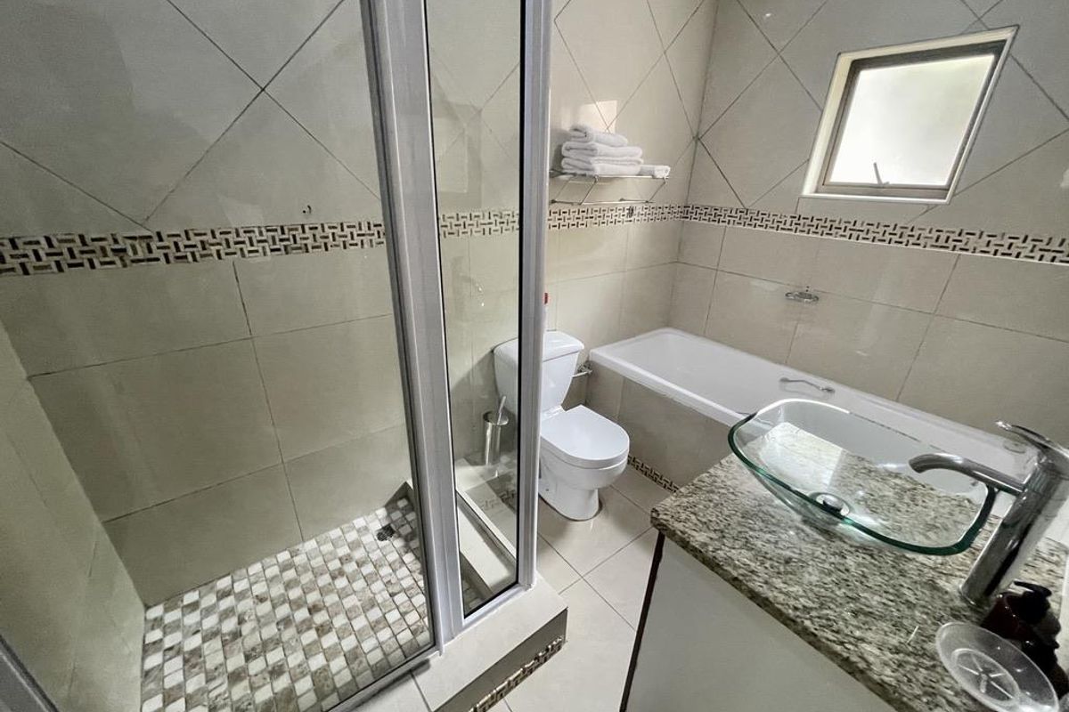 A functional bathroom featuring a glass-enclosed shower, a bathtub, a toilet, and a vanity with a glass vessel sink and granite countertop.