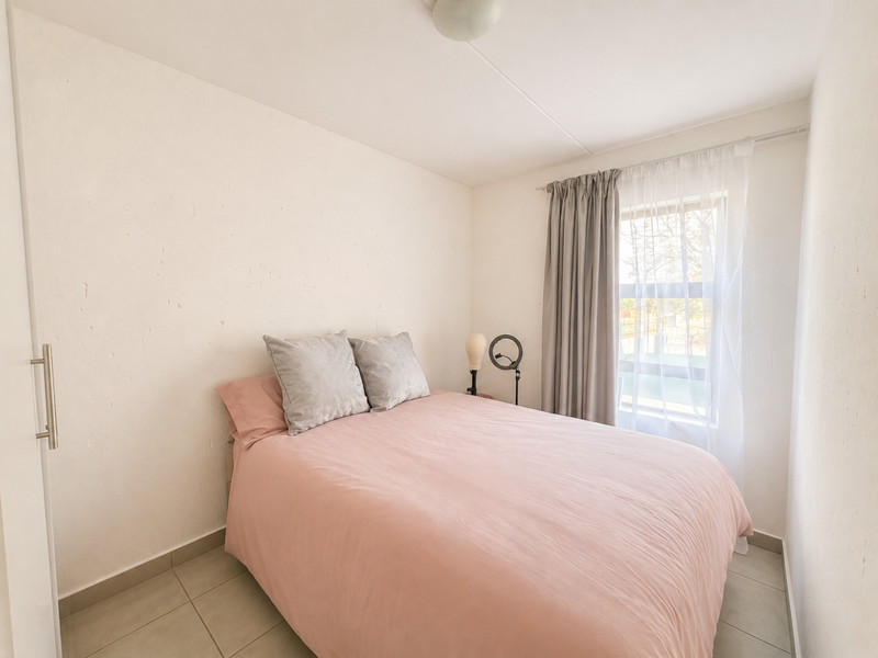 A compact bedroom featuring tiled flooring and a built-in cupboard, providing a functional space with natural light from the window.