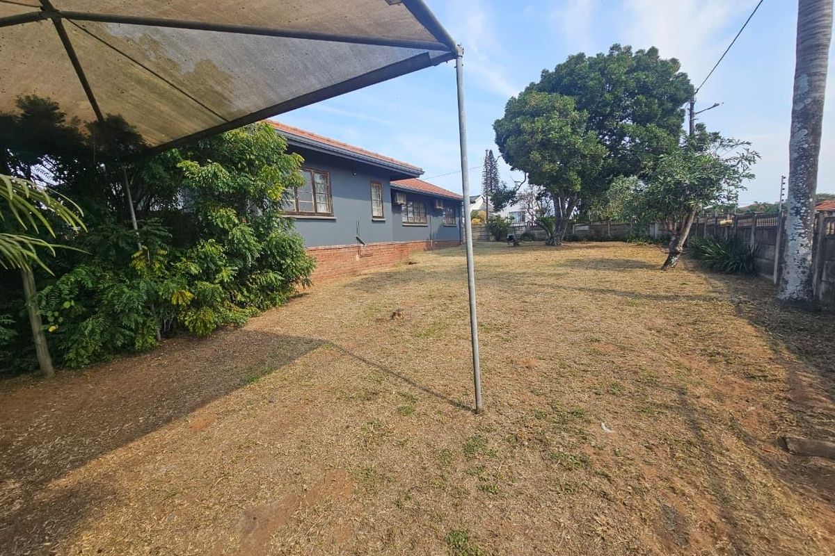 A spacious rear garden area featuring a large shade sail structure, established trees, and a brick perimeter wall.
