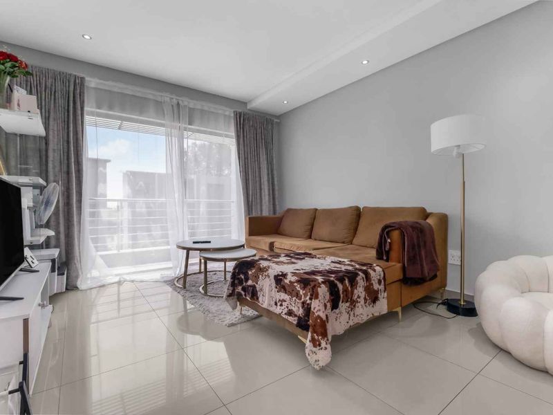 A bright and modern living room featuring large format floor tiles, recessed ceiling lighting, and a sliding glass door providing access to the balcony.