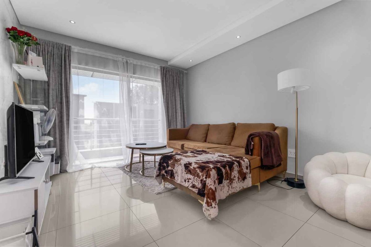 A bright and modern living room featuring large format floor tiles, recessed ceiling lighting, and a sliding glass door providing access to the balcony.