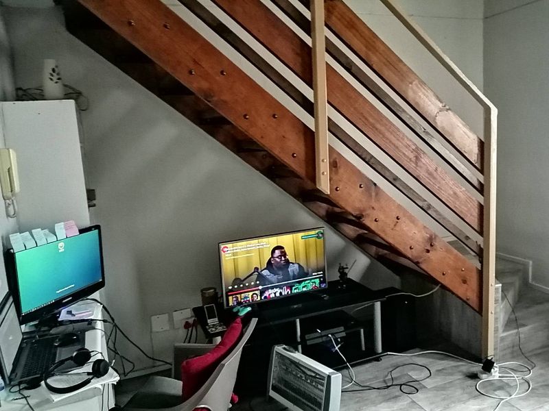 A living area featuring a wooden staircase with a simple railing and tiled flooring, providing a functional space under the stairs.