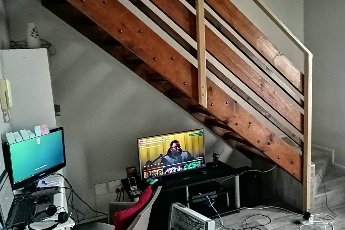 A living area featuring a wooden staircase with a simple railing and tiled flooring, providing a functional space under the stairs.