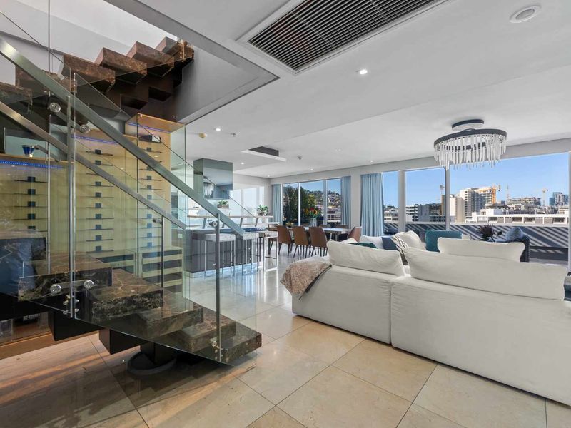 Spacious open-plan living area featuring a striking floating staircase with glass balustrade, built-in wine display, and floor-to-ceiling windows with expansive city views.