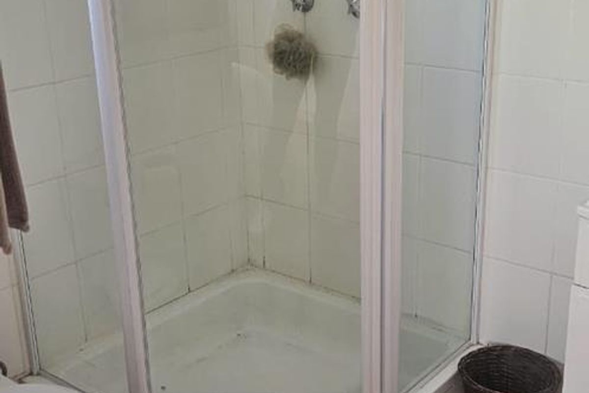 A functional bathroom featuring a corner shower enclosure with white wall tiling and terracotta-style floor tiles.