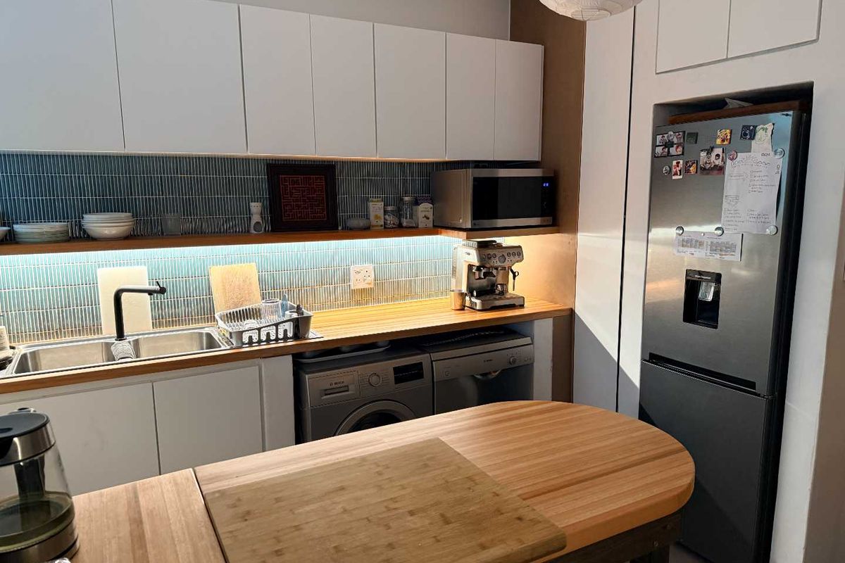 Modern kitchen featuring timber countertops, blue tiled backsplash, integrated appliances, and ample white cabinetry with under-cabinet lighting.