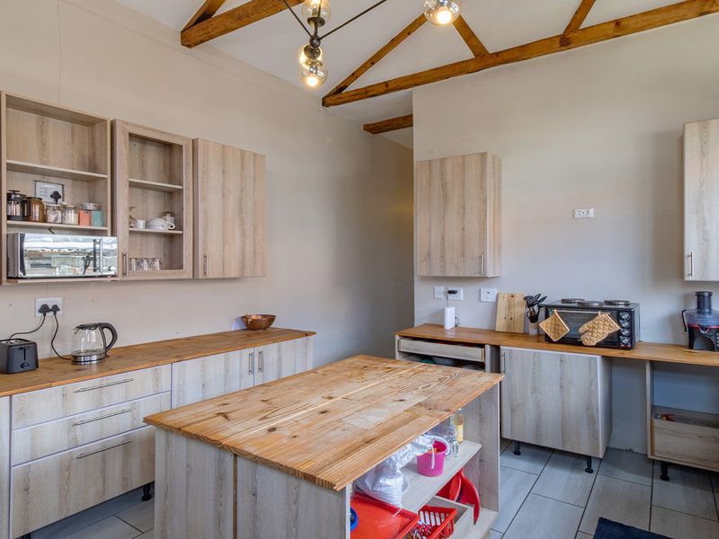 A functional kitchen featuring light wood-finish cabinetry, wooden countertops, a central island, and exposed timber ceiling beams, providing a rustic yet modern aesthetic.