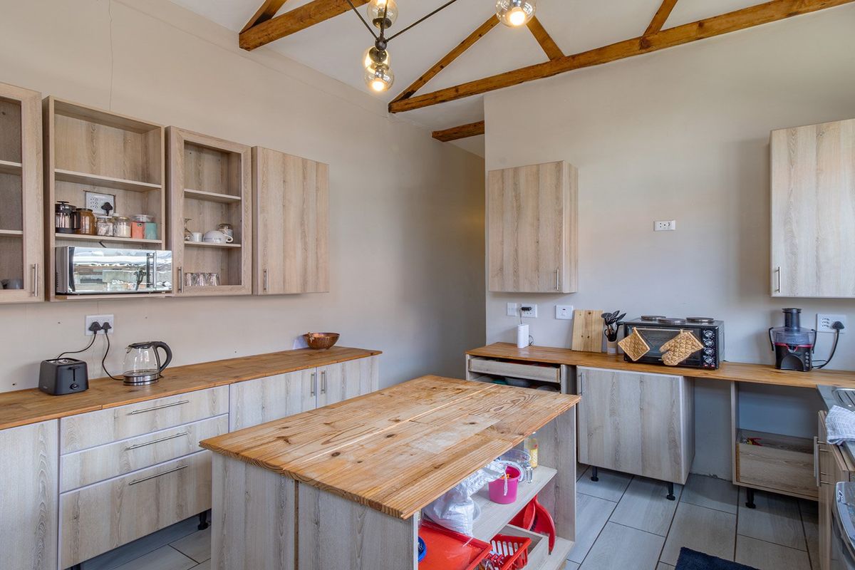 A functional kitchen featuring light wood-finish cabinetry, wooden countertops, a central island, and exposed timber ceiling beams, providing a rustic yet modern aesthetic.