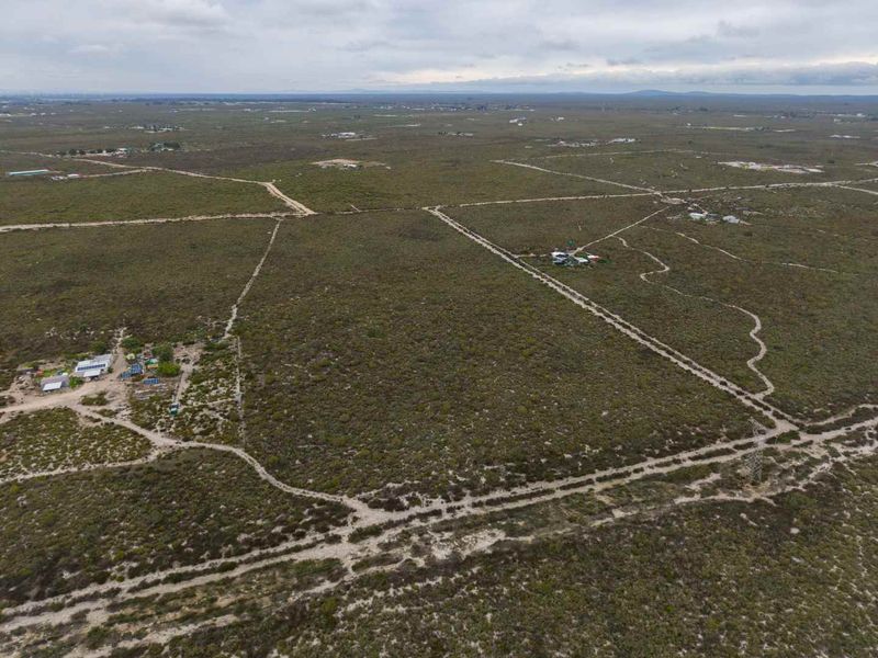 An aerial view of a large expanse of undeveloped agricultural land featuring dirt access roads and perimeter fencing.