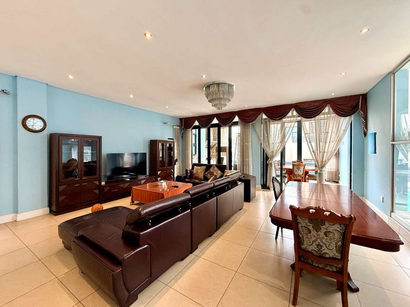 Spacious open-plan living and dining area featuring tiled flooring, recessed lighting, a decorative chandelier, and large sliding glass doors leading to the outdoors.