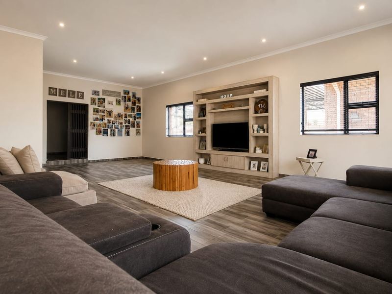Spacious living room featuring modern laminate flooring, recessed downlights, and a large built-in media unit with integrated shelving.