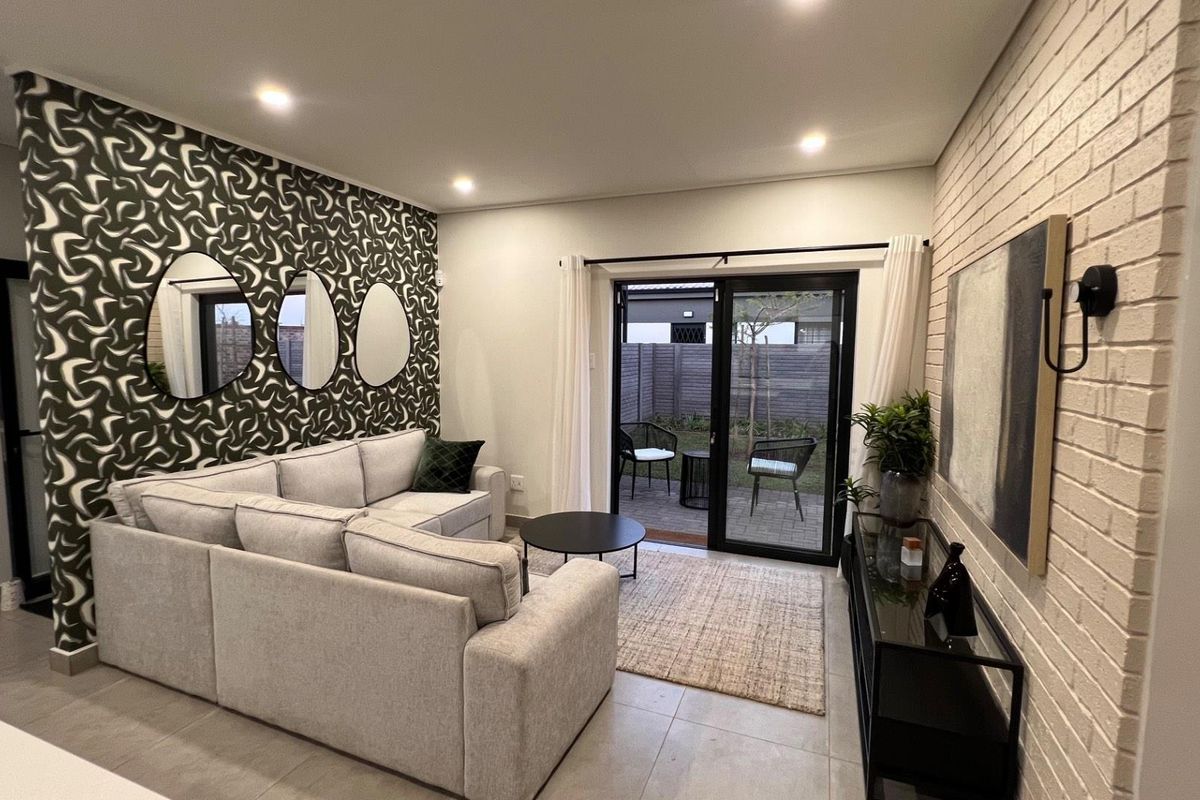 Modern living room featuring a textured brick feature wall, recessed downlighting, and large sliding glass doors providing direct access to a paved patio area.