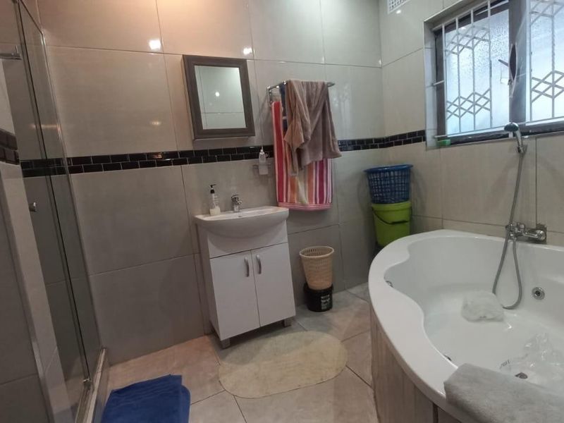 A functional bathroom featuring a corner spa bath, separate shower enclosure, vanity basin, and tiled finishes throughout.