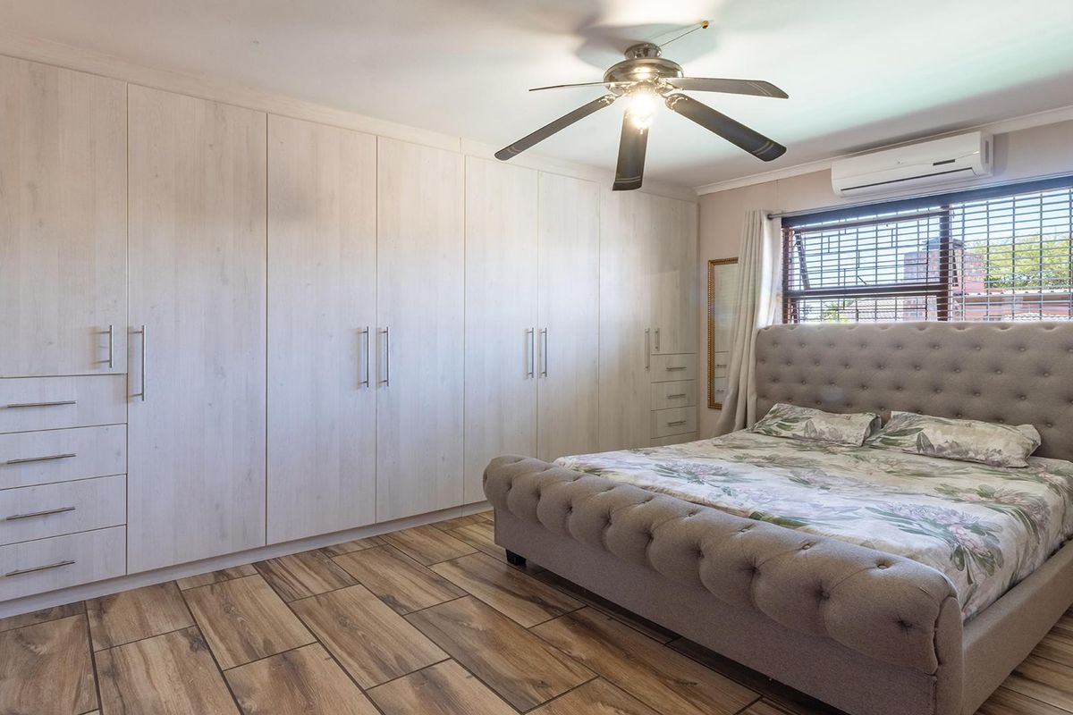 Spacious bedroom featuring extensive built-in cabinetry, wood-look tiled flooring, a ceiling fan, and a wall-mounted air conditioning unit.
