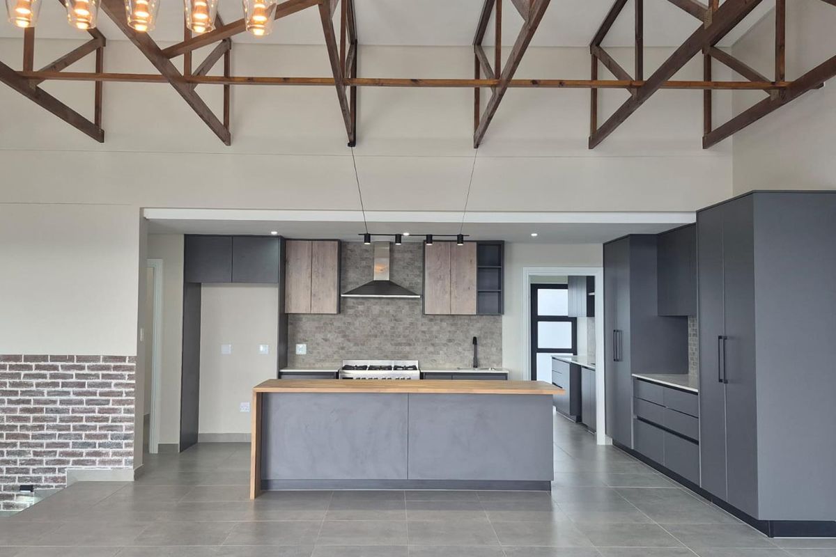 Modern open-plan kitchen featuring dark cabinetry, a central island with a wooden countertop, exposed timber roof trusses, and stylish pendant lighting.