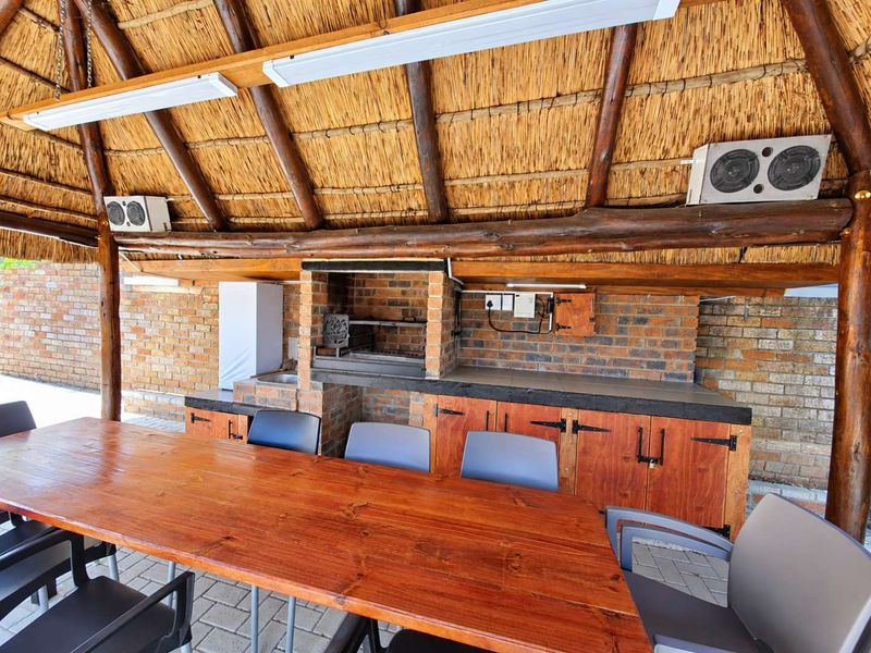 Covered outdoor entertainment area featuring a traditional thatched roof, exposed timber beams, and a built-in brick braai with integrated cabinetry and prep space.